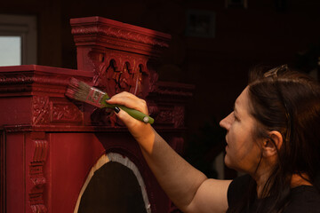Female having brush in hand and painting carved ornaments of massive antique cupboard made of wood....