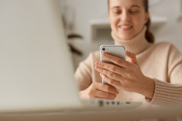 Closeup portrait of woman wearing beige sweater holding smart phone in hands, using cell phone for checking social networks, communicating online with friends.