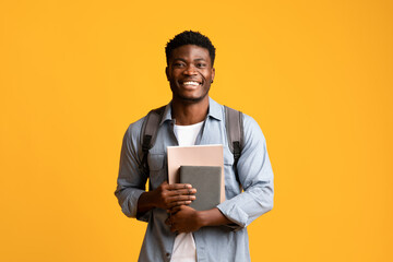 Positive african american guy student with books on yellow