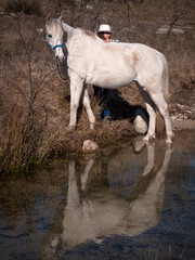 Female horse owner with white hat and her horse looking curiously to one side, reflection in water.