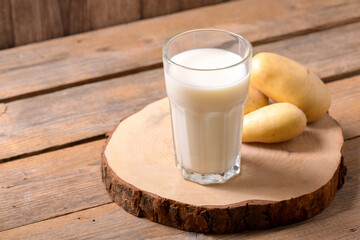 Vegan potato milk in a glass and potato tubers on brown wooden background. Close up. Plant based alternative milk replacer and lactose free, Trendy healthy vegetarian and vegan drink concept