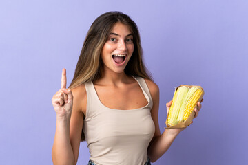 Young woman holding corn isolated on purple background pointing up a great idea