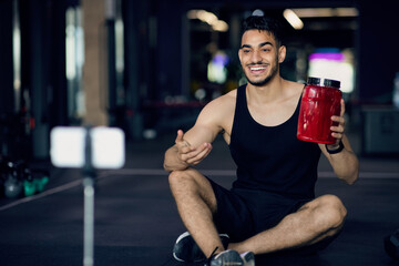 Fototapeta na wymiar Sporty Young Arab Man Making Video Review For Whey Powder At Gym
