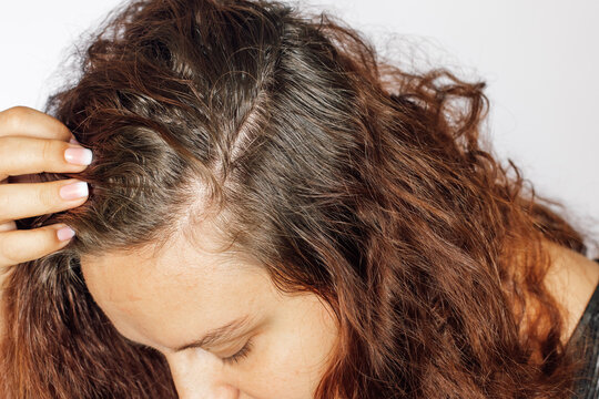 Closeup of young woman showing graying hair roots with head down on white background. Regrown roots which are in need of recoloring. Anti age care. Copy space.