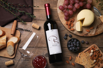 Bottle of red wine with glass and appetizers on wooden table, flat lay