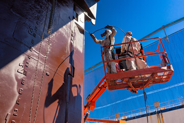 Painters painting a ship at a shipyard