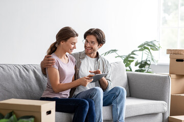 Obraz premium Smiling european young couple rest on sofa in living room interior with cardboard boxes and planning design