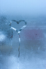 Naklejka na ściany i meble Closeup on love heart condensation inscription over sweaty window glass background. Valentine creative symbol concept. Hand draws heart on misty window