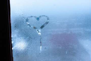 Obraz na płótnie Canvas Closeup on love heart condensation inscription over sweaty window glass background. Valentine creative symbol concept. Hand draws heart on misty window