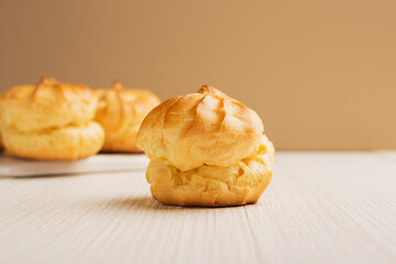 Freshly baked homemade profiteroles on a light wooden table. Traditional French dessert. Selective focus.