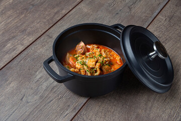 Still life of stewed tripe with chorizo in an iron casserole on a wooden board, typical cuisine of the city of Madrid. Traditional Spanish gastronomy concept.