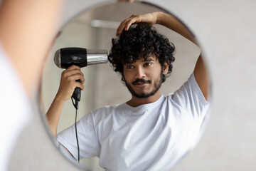 Handsome indian man drying hair after shower, making hairdo, taking care of himself in the morning