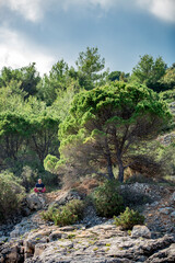 Digitaler Nomade mit Laptop sitzt in der Natur unter Bäumen und arbeitet, Hochformat