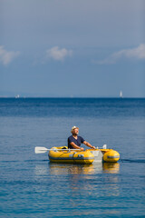 Mann mit Strohhut in gelbem Gummiboot irgendwo am Meer unterwegs, Hochformat