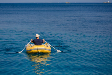 Mann mit Strohhut von hinten rudert in gelbem Gummiboot übers Meer, Nahaufnahme