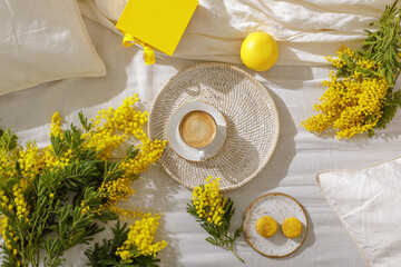 Branches of mimosa flowers on linen bed sheets, cup or coffee, french yellow macaroons, grapefruit and  gift box. Greeting for International Women's Day on March 8th, mother’s day or spring concept. - obrazy, fototapety, plakaty