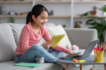 Happy asian girl doing homework, using laptop