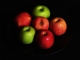 Fresh apples on a black porcelain plate on black background.