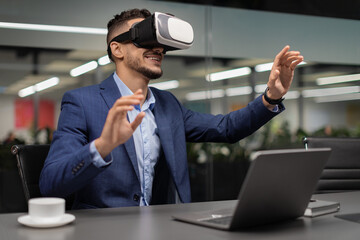 Excited businessman sitting at workdesk, using VR glasses