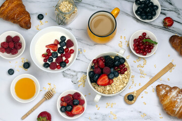 Healthy breakfast with cup of coffee, yogurt of fruit, oat with berry, honey and ripe sweet berries on white marble background top wave, flat lay.