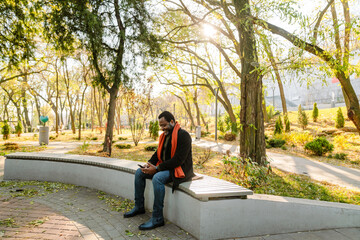 Black bearded man using cellphone while sitting on bench