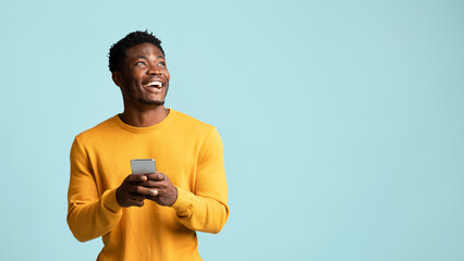 Cheerful black man using smartphone, looking at copy space