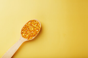 Vitamin D3 Capsules in a spoon with other vitamin D3 capsules around them on a yellow background