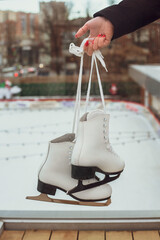 A young woman holds ice skates in her hands against the background of an ice rink