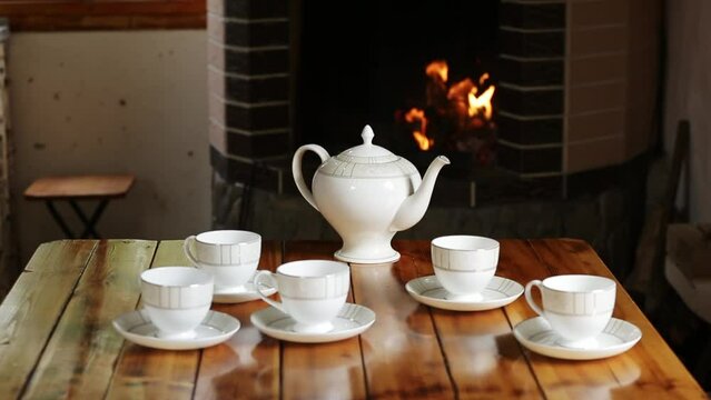 A white porcelain tea set stands on a wooden table against the background of a fire burning in the fireplace in the dwelling of the Caucasian highlanders
