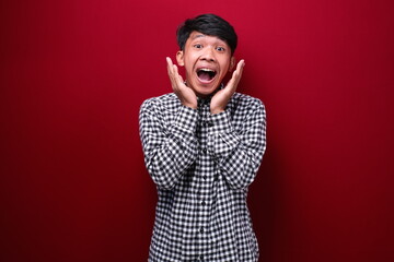 asian man wearing plaid shirt with shocked expression, on red background