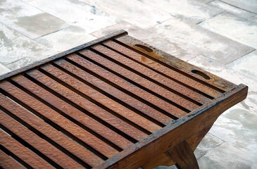 Morning dew on a wooden sunbed close-up against the background of the street pavement