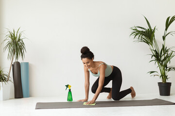 Smiling young female using sanitizer and wet wipe to clean yoga mat