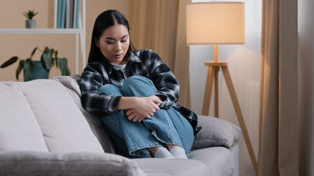 Sad worried asian korean woman having psychological problem sitting on sofa couch feeling alone anxiety depression japanese girl upset frustrated at home grief troubled unwanted pregnancy boredom
