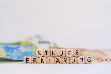 German word for tax return, STEUERERKLÄRUNG, spelled with wooden letters wooden cube on a plain...