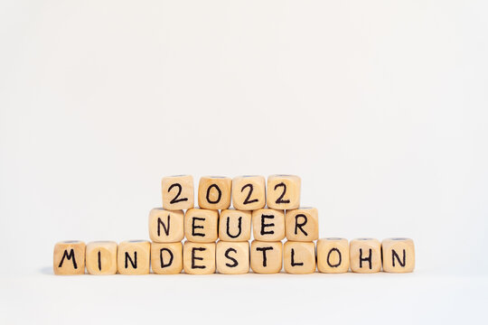 2022 German word for Minimum wage, MINDESTLOHN, spelled with wooden letters wooden cube on a plain white background with banknotes, concept image