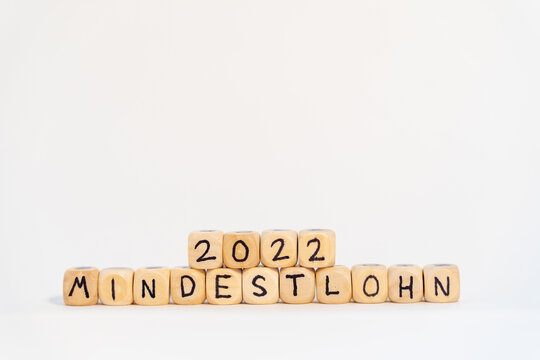 2022 German word for Minimum wage, MINDESTLOHN, spelled with wooden letters wooden cube on a plain white background with banknotes, concept image