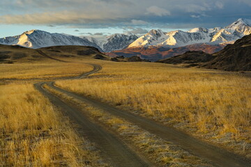 Russia. The South of Western Siberia, the Altai Mountains. A dirt road going into the mountains against the background of the snow-covered North Chui mountain range near the village of Kurai.