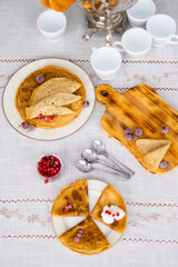 Russian traditional pancakes or blini with sour cream and red currant berries on table laid for...