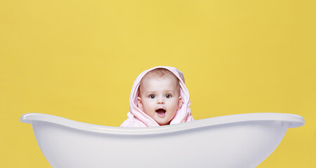 Just washed adorable baby in pink bathrobe on bright yellow background. Free space for text. Child...