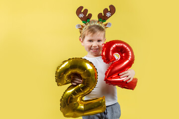 Happy funny child boy in red Christmas reindeer costume with balloon numbers