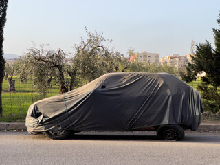 Unrecognizable car covered with protective cloth outdoors