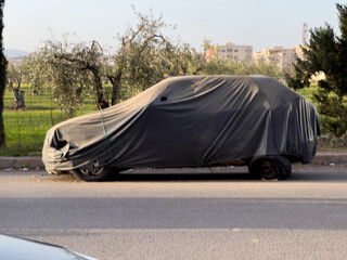Unrecognizable car covered with protective cloth outdoors