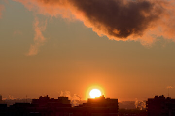 Naklejka premium Cityscape at sunset . The sun sets over the horizon over the rooftops. Photo of the city in the golden hour.