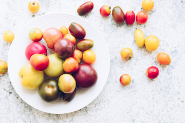 Various colorful tomatoes on white plate on stone table