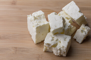 Soft white cheese cubes on wooden board with copy space
