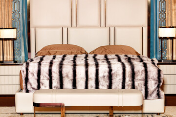 Beautiful stylish bedroom interior with a wide bed, bedside tables and a striped fur cape in calm beige tones.