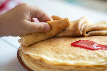 Child's hand takes a thin pancake from a plate