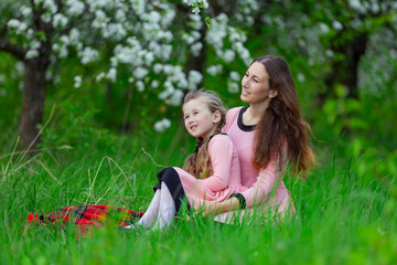 mother and daughter sit in the apple orchard in spring