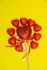 Chocolate red heart sweets for Valentine's Day on a yellow background in the shape of a circle with a heart decoration on a wooden pole in the middle.
