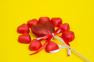 Chocolate red heart sweets for Valentine's Day on a yellow background in the shape of a circle with a heart decoration on a wooden pole in the middle.